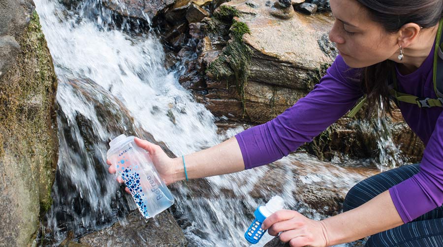 Woman filling up a water filter from a waterfall