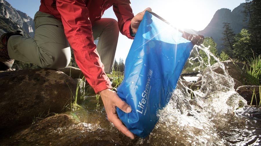 Man filling a lifestraw water filter bladder from a river bank