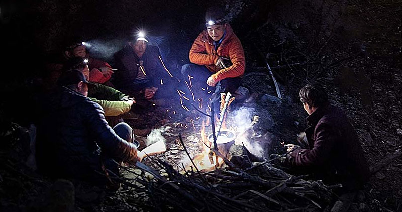 Men with headlamps at night sitting around a campfire