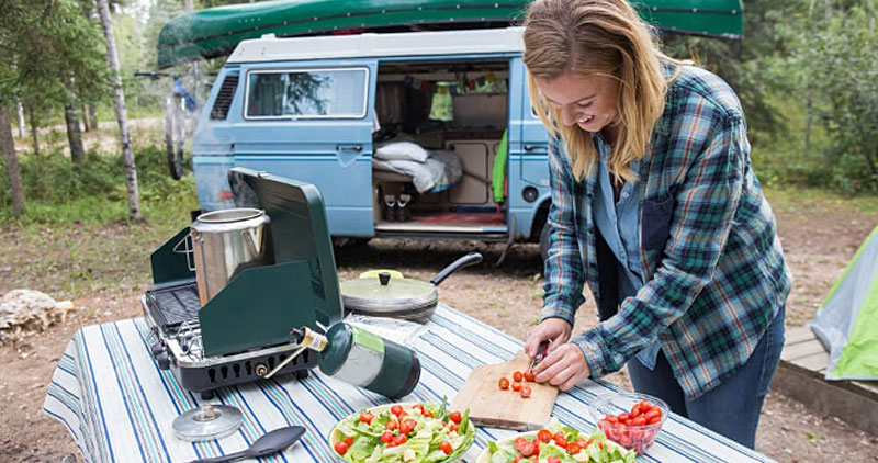 Woman making a salad at a campsite in front of an Volkswagen camper