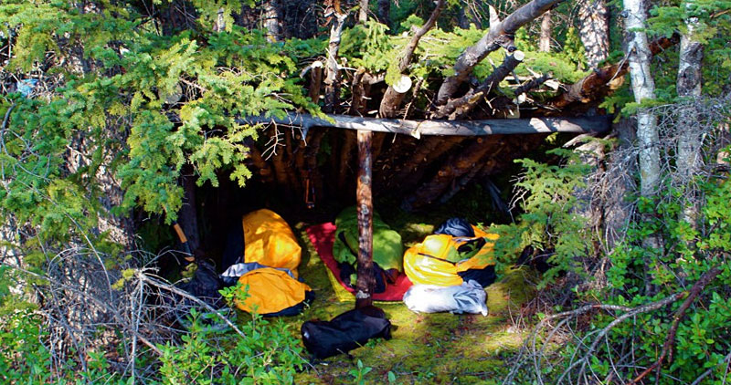 Canadian Wilderness School & Expeditions: backpacks and sleeping bags setup in a bushcraft shelter made of pine branches