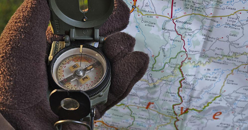 A gloved hand holding a lensatic compass with a map in the background