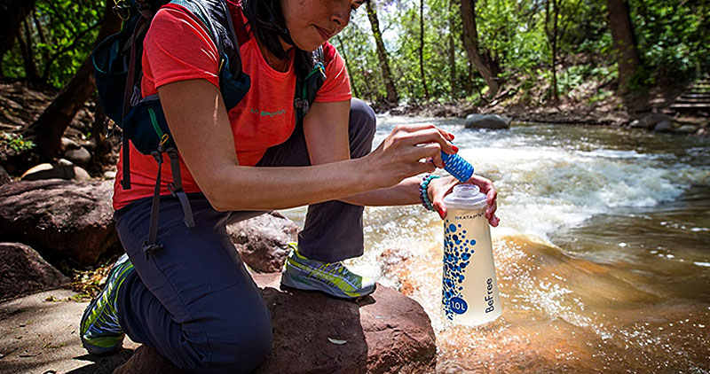 A woman filling a Katadyn BeFree 1.0L Water Filter from a river in the woods
