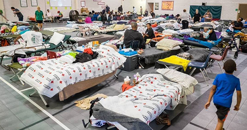 Cots in an emergency storm shelter with people and their belongings