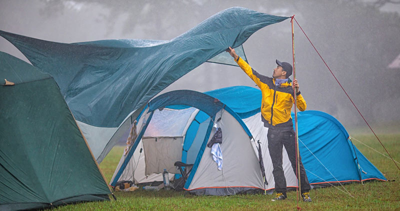 A man trying to fix a tarp in a rain storm which is blowing away