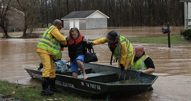 Woman being helped out of a boat in a flood by emergency workers