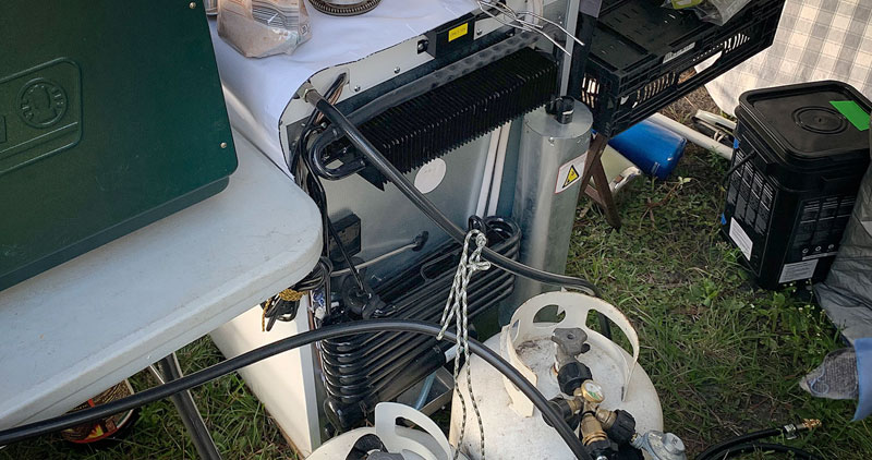 The back of a propane refrigerator with a propane tank nearby
