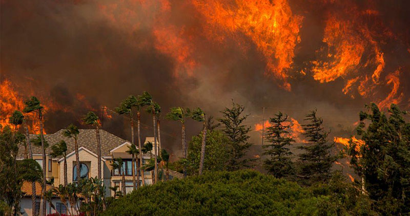 A huge wild fire encroaching on a large home