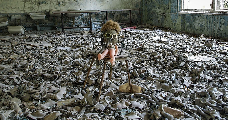 A doll wearing a gas mask in a room full of old dirty gas masks scattered across the floor