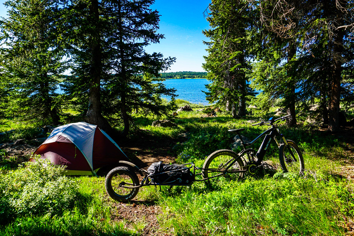 QuietKat All Terrain Electric Bike with trailer in a campsite next to a lake in the woods