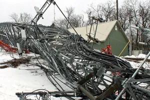 A collapsed cell phone tower next to a house in the snow