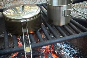 A steel pot and cup on a metal grate over a campfire