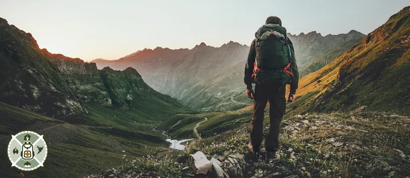 A man wearing a backpack standing in a valley looking at some mountains