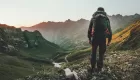 A man wearing a backpack standing in a valley looking at some mountains